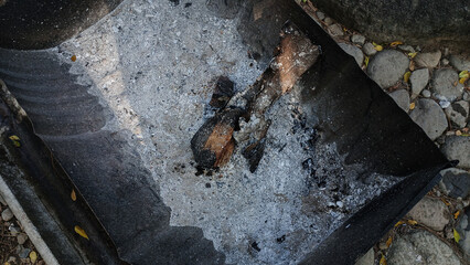 Charred wood and white ash remain in a metal container after a fire has burned out, surrounded by...