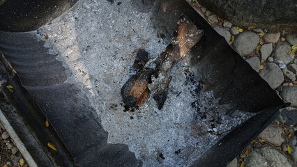 Charred wood and white ash remain in a metal container after a fire has burned out, surrounded by...