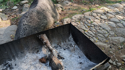 Charred wood and white ash remain in a metal container after a fire has burned out, surrounded by...