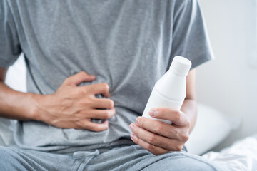 Man Stomachache and Discomfort, Holding a bottle of Antacid Gel in His Hand to Relief  Acid Reflux,...