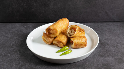 Sosis Solo (Sausage Solo). Special designation for a chicken dish wrapped in an omelet and shape like sausagea. Traditional Indonesian meat snack, served on a white plate with green chili garnish.