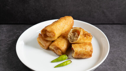 Sosis Solo (Sausage Solo). Special designation for a chicken dish wrapped in an omelet and shape like sausagea. Traditional Indonesian meat snack, served on a white plate with green chili garnish.