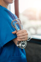 Close-up of a healthcare worker in blue scrubs holding a stethoscope, symbolizing medical care and professionalism.