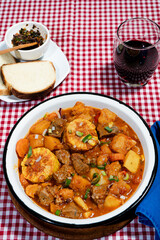 Hearty beef stew called carbonada simmering with vegetables and corn on the cob, served with bread and wine