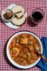 Beef stew called carbonada with potatoes, corn, and carrots served on gingham tablecloth with wine and bread