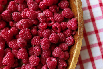 A wooden bowl with ripe raspberries lies on a rustic tablecloth.