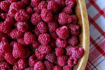 A wooden bowl with ripe raspberries lies on a rustic tablecloth.