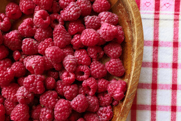 A wooden bowl with ripe raspberries lies on a rustic tablecloth.