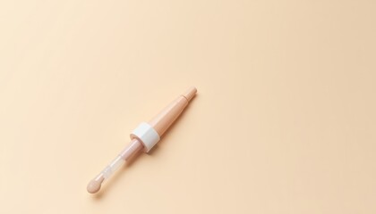 Fototapeta premium Light beige cosmetic concealer applicator on a pale peach background.