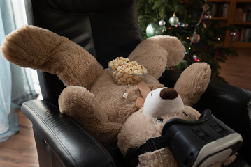teddy bear wearing VR glasses lies with popcorn on his stomach