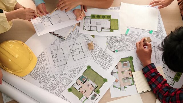 Architect and safety engineer discussion about building construction use blueprint on table with architectural document, measurement tool and wooden block scatter around at modern office. Delineation.