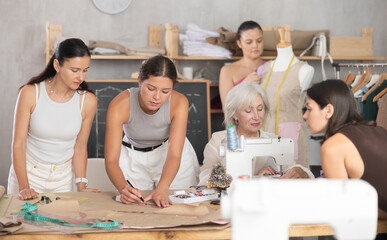 Group of women sew, draw pattern on paper and work with mannequin at sewing workshop