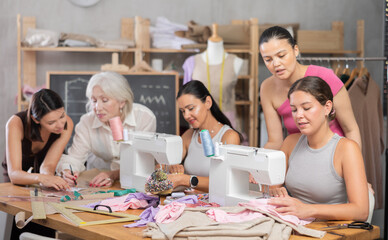 Group of women sewing on machine and draw pattern on paper during lesson at sewing workshop