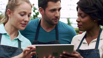 Three people looking at a tablet with aprons on in an outdoor setting together - Powered by Adobe
