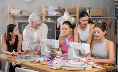 Group of women sewing on machine and draw pattern on paper during lesson at sewing workshop