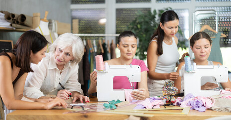 Group of happy attendees of dressmaking courses sewing and drawing with curves controlled by master