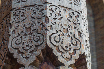 An old hexagonal wooden column with carved patterns and figures. Decorative elements in the...