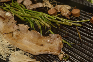 불판 위에서 삼겹살, 버섯, 소시지를 함께 굽는 모습
