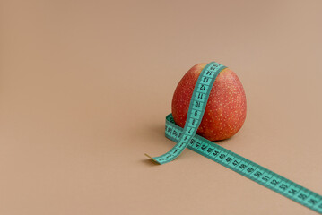 An apple with a measuring tape on a brown background with space for text. The concept of weight...