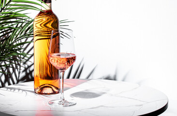 stylish glass filled with rose pink wine beside a bottle on a marble table, surrounded by soft...