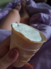Hand holding ice cream against the background of feet in bed