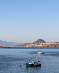  Boats float on calm blue waters, with coastal towns and rugged mountains under a clear sky,...