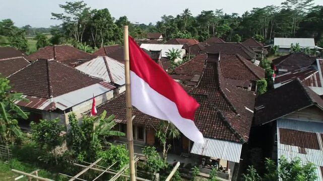 Indonesian flag waving over rooftops in a rural area