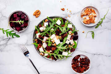 Gourmet beet salad with soft cheese, arugula, raisins and walnuts, marble table background, top view