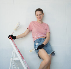 Young woman painting indoors wall with roller using stepladder