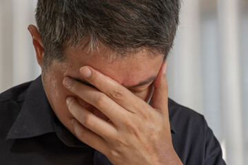 An Asian man clutches his head, showing signs of work-induced psychological stress—potentially...
