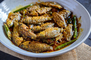 Bengali-style puti fish jhal served in a bowl – spicy small fish curry, traditional Bengali non-veg dish, puti macher jhal, Indian freshwater fish in mustard gravy, homestyle overhead view
