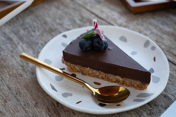 A slice of chocolate cake garnished with blueberries and herbs, served on a decorative plate with a...