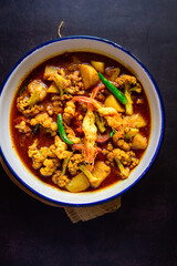 Traditional Bengali-style prawn curry with potato and cauliflower garnished with green chillis – Indian seafood curry, authentic Bengali chingri recipe, homestyle jhol, rustic comfort food, top view