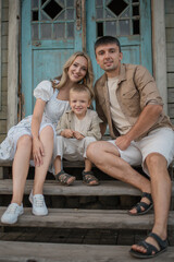 A young family, mom, dad, and a little son, are sitting on the porch of their house.