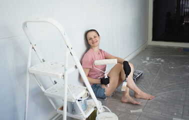 Young woman painting indoors wall with roller using stepladder