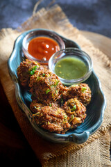 Peyaji or Peyaju – crispy Bengali lentil onion fritters served with tomato chutney and green chilli sauce on rustic jute fabric – Indian street food snack, monsoon comfort food, traditional cuisine