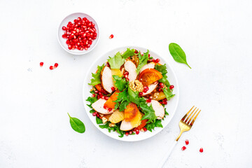 Autumn salad with grilled chicken, persimmon, pomegranate, walnuts, oranges and lettuce, top view