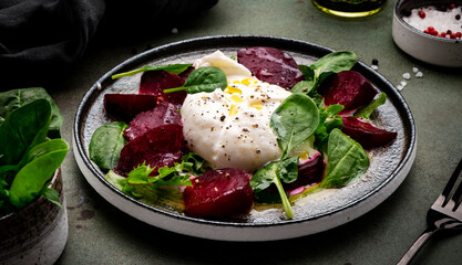 Gourmet salad with burrata cheese, baked beets, spinach and olive oil, green stone background, top view