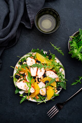 Juicy salad with grilled chicken fillet, orange slices, raisins, walnut, arugula, spinach and useful seeds, black table background, top view