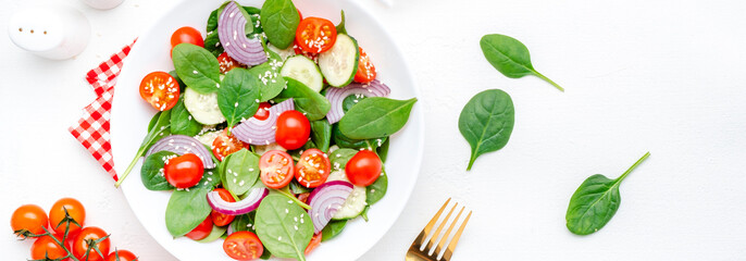 Healthy vegan vegetable salad with spinach, tomatoes, cucumber, onion, sesame seeds and olive oil. White table background, top view