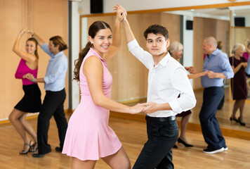Obraz premium Happy attractive young girl enjoying impassioned merengue with guy partner in latin dance class. Social dancing concept