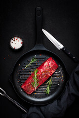 Fresh raw beef sirloin meat with rosemary and spices on grill pan with knife and fork for meat....