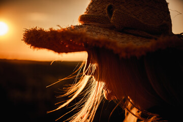 Close-up of a teen girl in a straw hat at sunset, warm light highlighting her hair and profile in a...