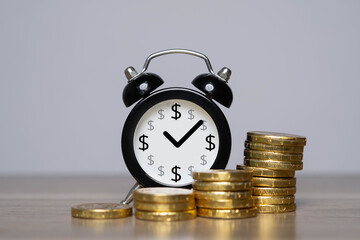 A black alarm clock with dollar signs and a check mark stands beside stacks of golden coins,...
