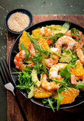 Seafood salad with shrimps, avocado, fresh orange, arugula and white sesame seeds on green stone background. Top view