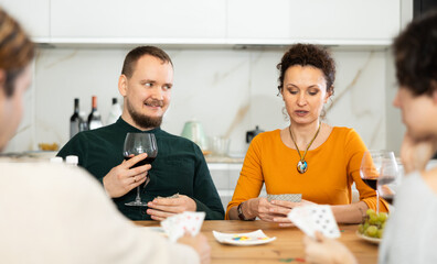Happy group of friends playing poker cards and drinking wine at home