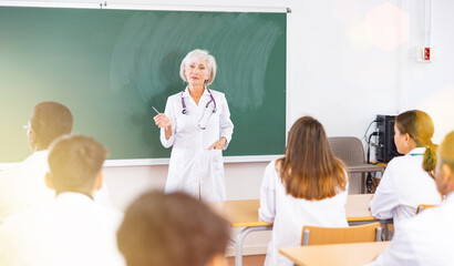 Experienced elderly female professor of medicine giving lecture to group of young adult students at...