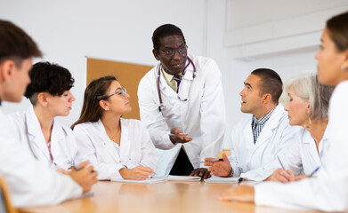 Group of medical students in white coats studying in classroom. African-american man professor...