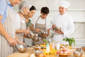Positive adult man professional chef conducting culinary courses, imparting cooking skills to diverse group of people of different ages..