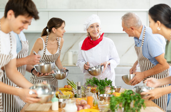 Adult students prepare food according to recipe in cooking class led by a female chef